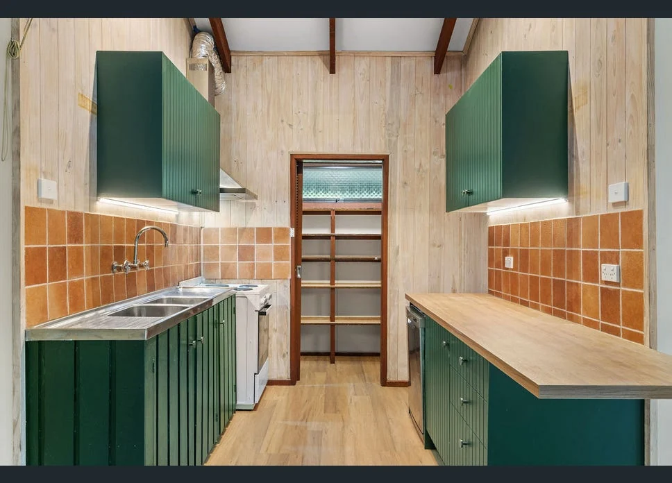 Beach house kitchen with deep green cabinetry, timber worktop and terracotta tiled splashback